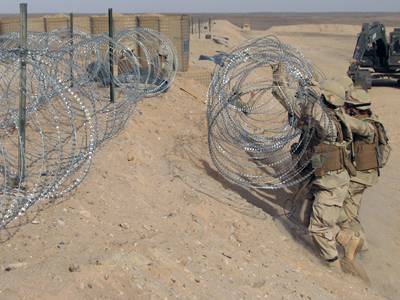 Several soldiers are installing the concertina razor wire in the military site.