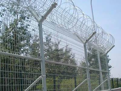 Several pieces of galvanized curvy welded wire mesh fences with razor wires on the top of the fence.