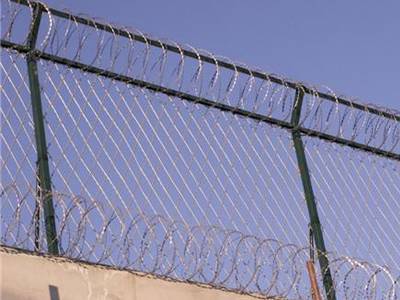 Straight razor wire fences on the wall with concertina wires at the top and bottom of fence.