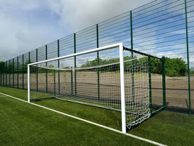 A green PVC welded football fence with square posts is installed on a piece of grassland.