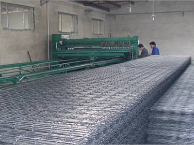 Long and wide welded wire mesh panels are in the workshop, two workers are handling the machine.