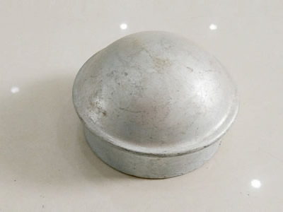 A galvanized metal post cap on the ground.