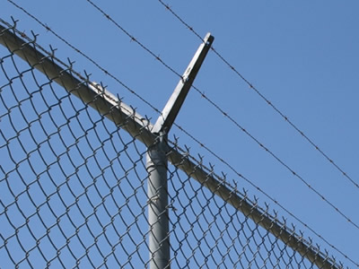 Single arm extension with barbed wire is on the round post, which is fastening chain link fence.