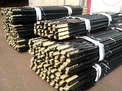 Several bundles of black bitumen coated T studded posts on the ground.