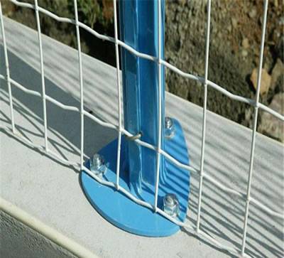 A piece of white Euro fence is fixed on the concrete ground with bolts and nuts.