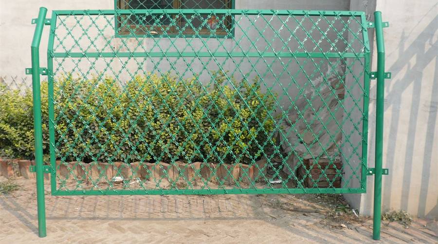 A piece of green color straight razor wire fence is raised by the round post.