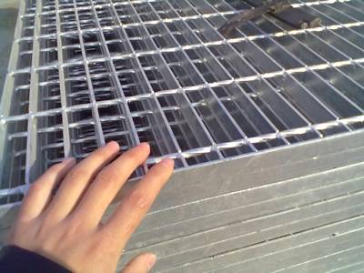 A hand is placed on a stack of galvanized welded steel grating.