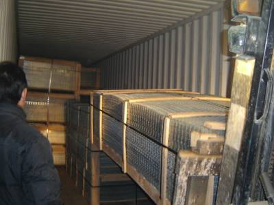 Workers are loading welded wire mesh panels into the container with a forklift